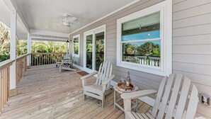 Eine überdachte Veranda mit Holzboden, weißen Adirondack-Stühlen und einem Tisch mit einer Flasche und einem Glas.