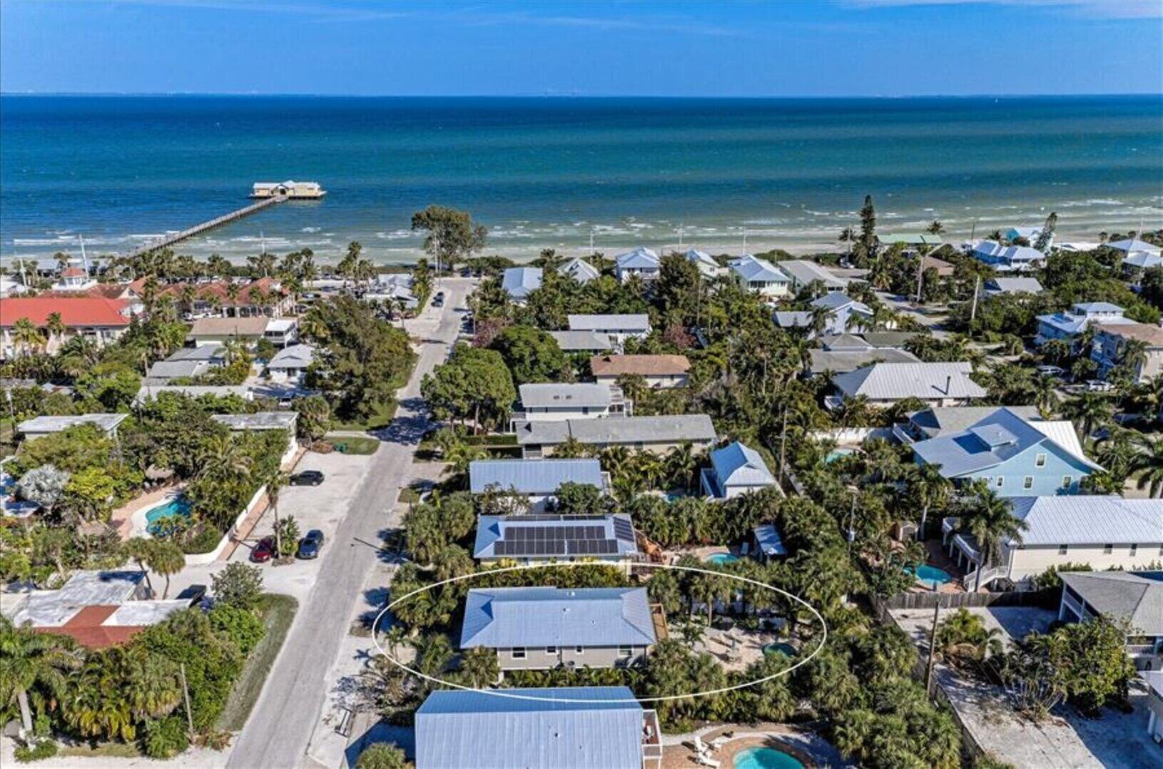 Vue aérienne d’un quartier résidentiel situé sur la côte, avec des maisons, une jetée et une piscine.