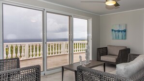 A balcony with a view of the sea, wicker furniture, and a ceiling fan.