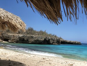 A beach with clear turquoise water, rocky outcrops, and a thatched structure. - Luxury living, private pool and spectacular views! (Sabadeco)