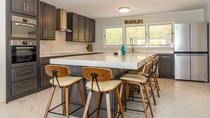 A modern kitchen with dark cabinets, stainless steel appliances, and a central island with bar stools.
