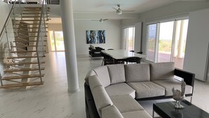 A spacious living area with a large sectional sofa, a glass coffee table, and a staircase with glass railings.