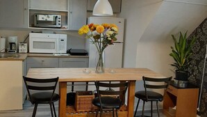 Una cocina compacta con electrodomésticos blancos, una mesa de comedor con cuatro sillas y un florero con flores.