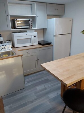 A compact kitchen with white cabinets, a microwave, a toaster, and a refrigerator.