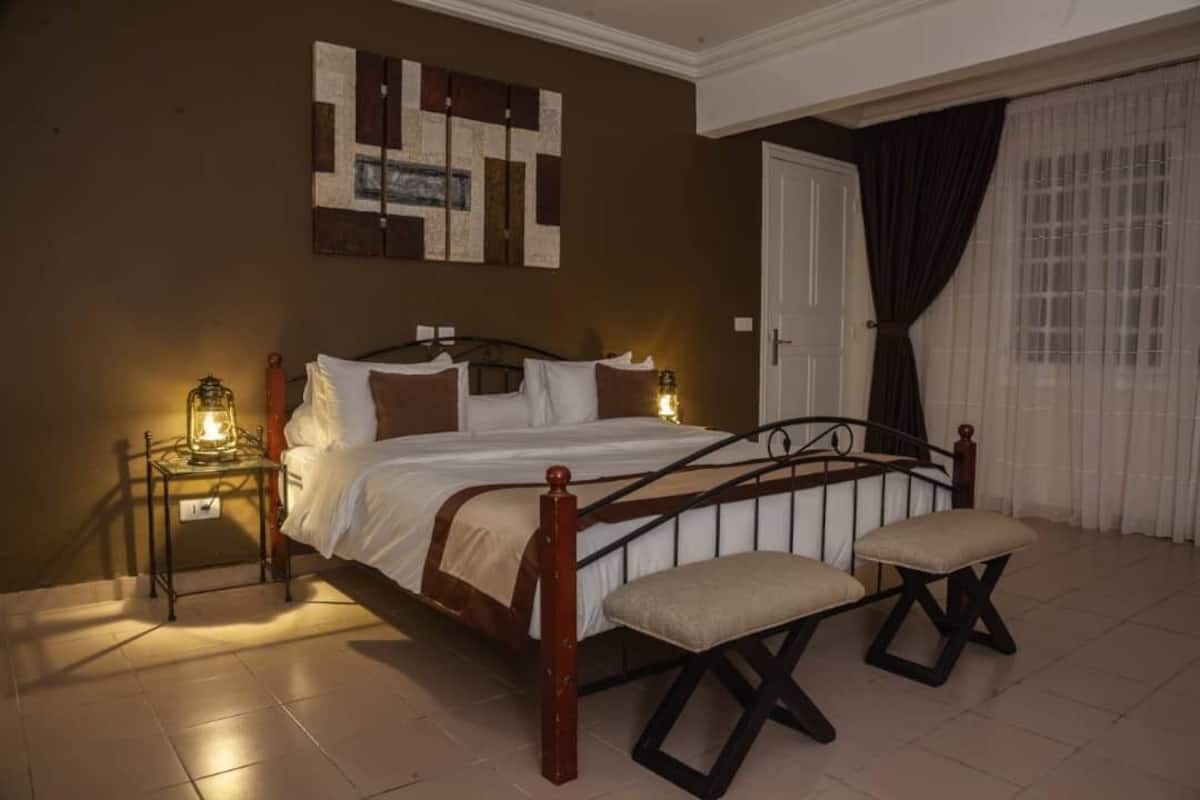 A bedroom with a bed, bedside tables, a bench, and a wall art piece.
