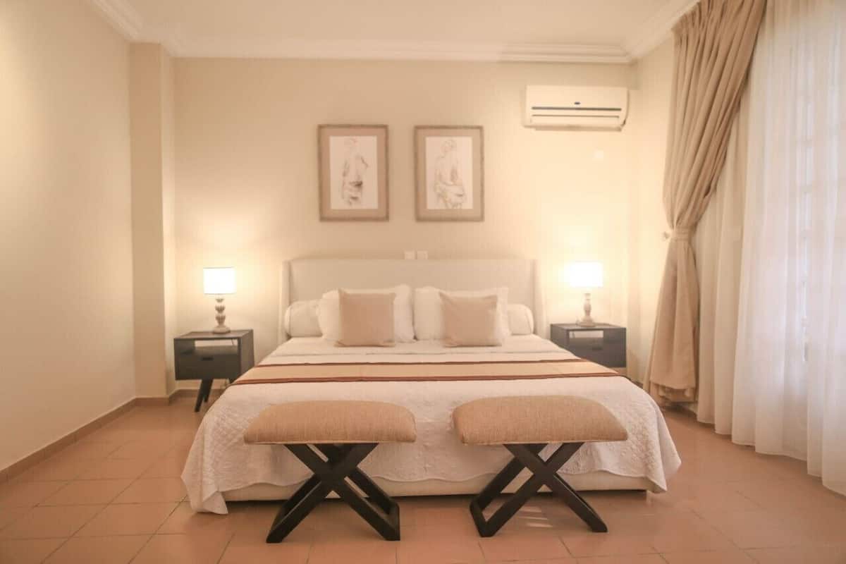 A hotel room with a large bed, two bedside tables with lamps, a headboard, and two framed pictures on the wall.