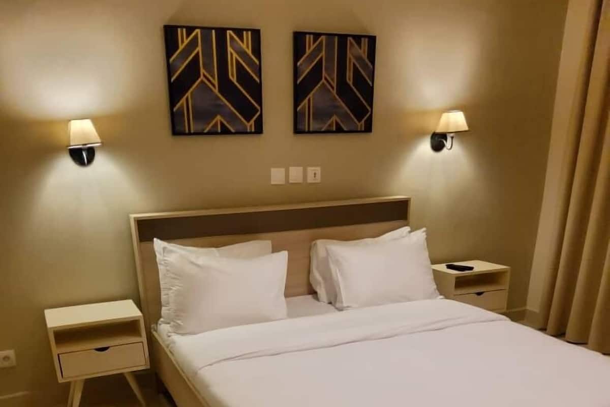 A hotel room with a large bed, two bedside tables, and two wall-mounted lamps.