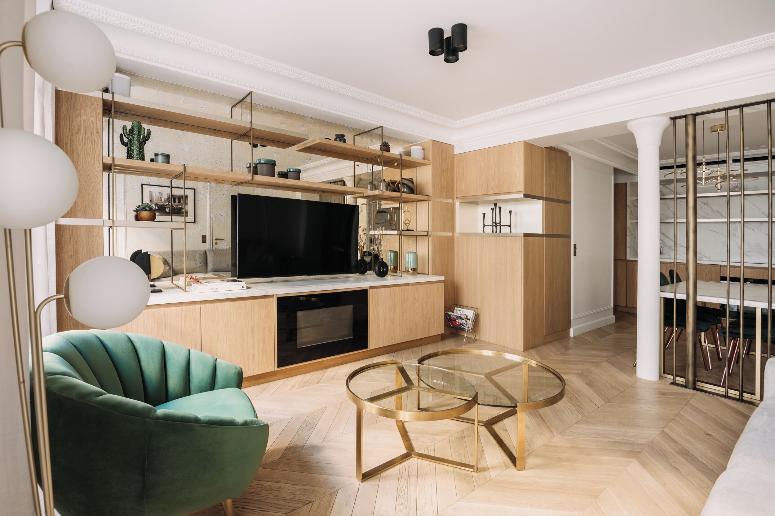 A modern kitchen with wooden cabinets, a built-in TV, and a dining area with a glass table and chairs.