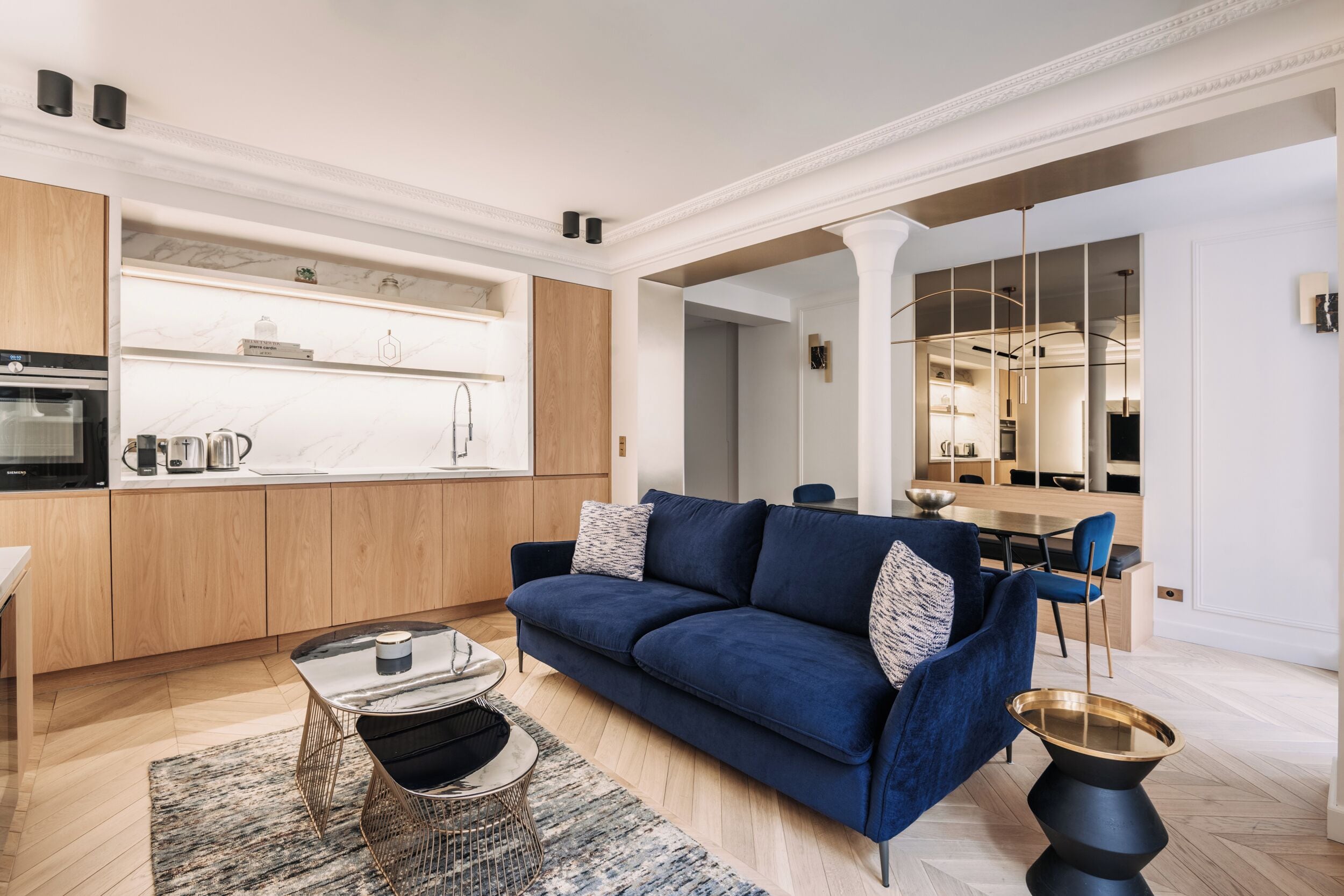 Een moderne woonkamer met een blauwe bank, een bijzettafeltje en een eethoek op de achtergrond.