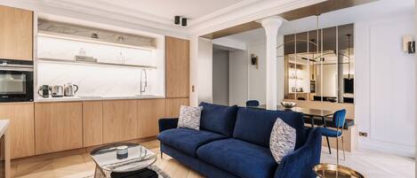 Een moderne woonkamer met een blauwe bank, een bijzettafeltje en een eethoek op de achtergrond.