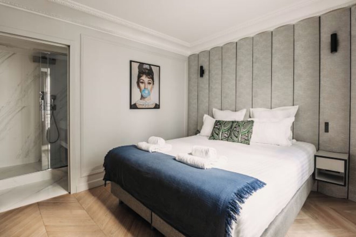 A modern hotel room with a large bed, a shower, and a framed picture on the wall.