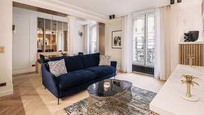 A modern living room with a dark blue sofa, a glass coffee table, and a white console table with decorative items. - HIGHSTAY - Luxury Serviced Apartments - Louvre-Rivoli (Paris)
