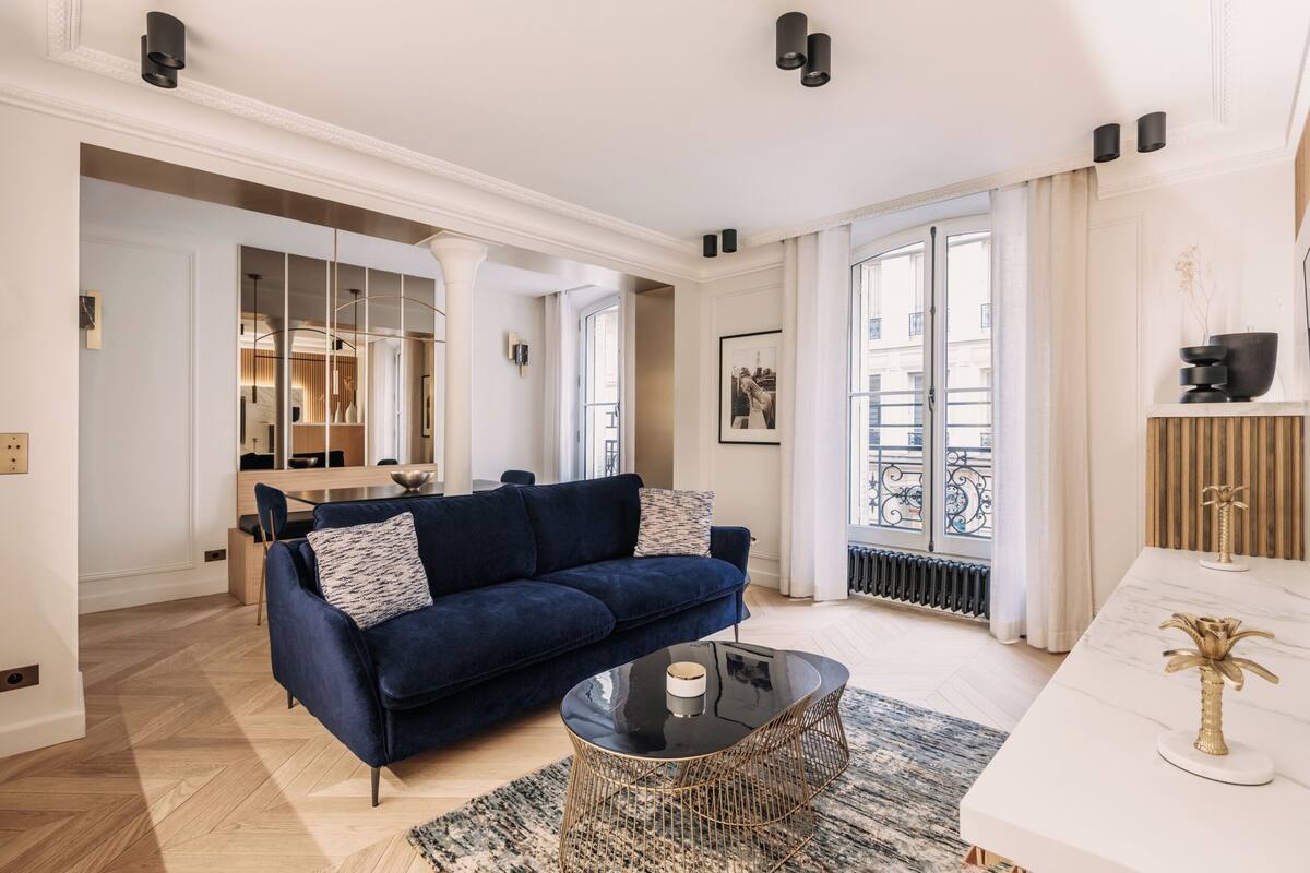 A modern living room with a dark blue sofa, a glass coffee table, and a white console table with decorative items.