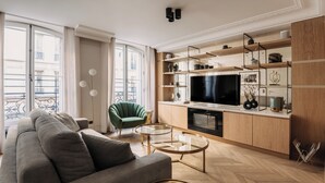 A modern living room with a sofa, a green armchair, a glass coffee table, and a TV. - HIGHSTAY - Luxury Serviced Apartments - Louvre-Rivoli (Paris)