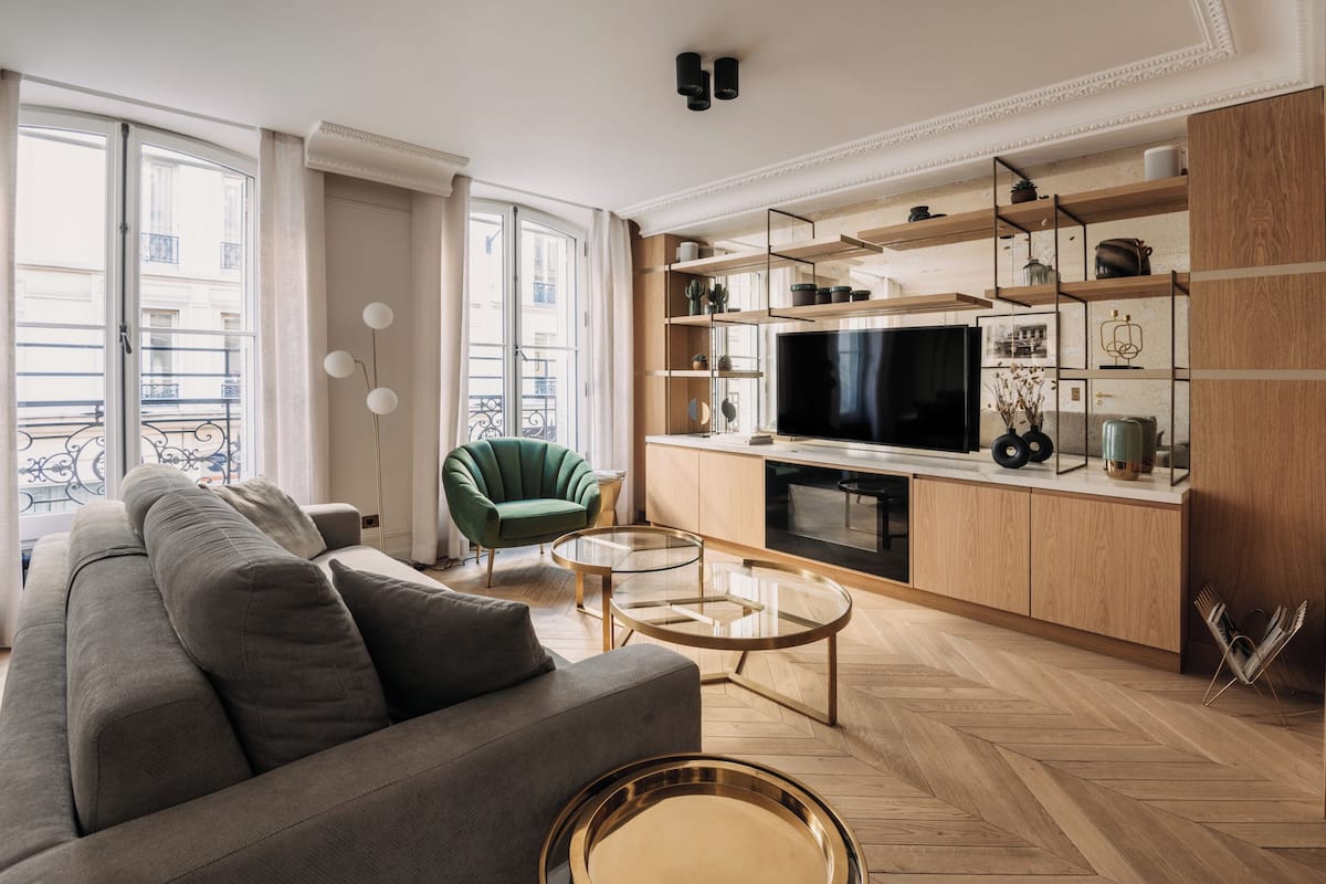 A modern living room with a sofa, a green armchair, a glass coffee table, and a TV.