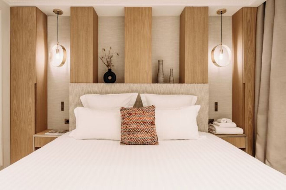 A hotel room with a large bed, wooden panel walls, two bedside lamps, and a nightstand with a telephone.