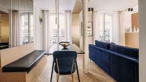 A modern living room with a dark blue sofa, a wooden bench, and a dining table with a bowl. - HIGHSTAY - Luxury Serviced Apartments - Louvre-Rivoli (Paris)