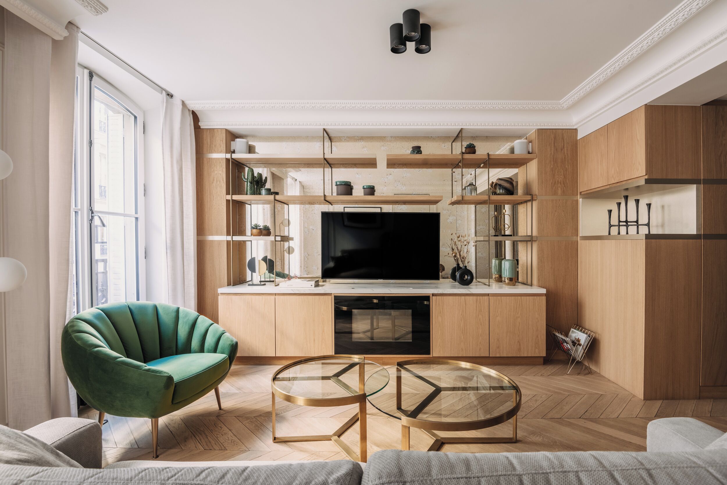 Een moderne woonkamer met een groene fauteuil, een glazen salontafel en een flatscreen televisie.