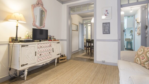 A room with a white dresser, a television, a mirror, and a sofa. There is a door leading to another room.