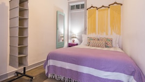 A bedroom with a bed, a hanging shelf, a mirror, and a door.