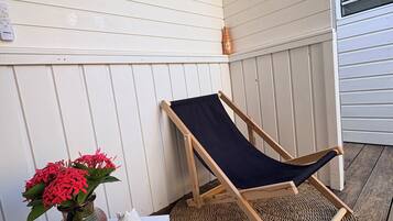A wooden deck with a single black lounge chair, a small table with a vase of red flowers, and a sign on the wall.