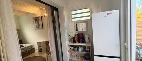 A compact kitchen with a refrigerator, coffee maker, and shelves with kitchenware.