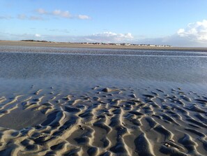 A beach with sand patterns and a distant shoreline with buildings.