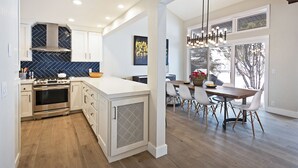 Een moderne keuken met witte kasten, een groot eiland en een eethoek met een houten tafel en stoelen.