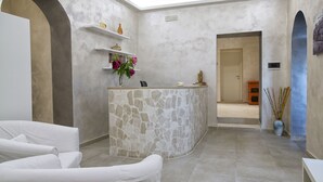 A reception area with a stone counter, white sofas, and a vase of flowers. - Relais La Pretura (Vieste)