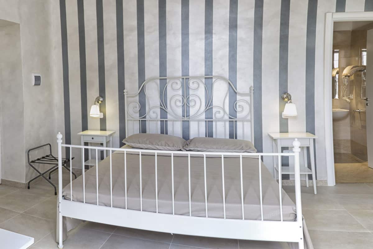 A bedroom with a white metal bed frame, a striped wall, and a bathroom visible through an open door.