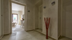 A hallway with a door leading to a bedroom, a bathroom, and a sitting area with a chair and table. - Relais La Pretura (Vieste)