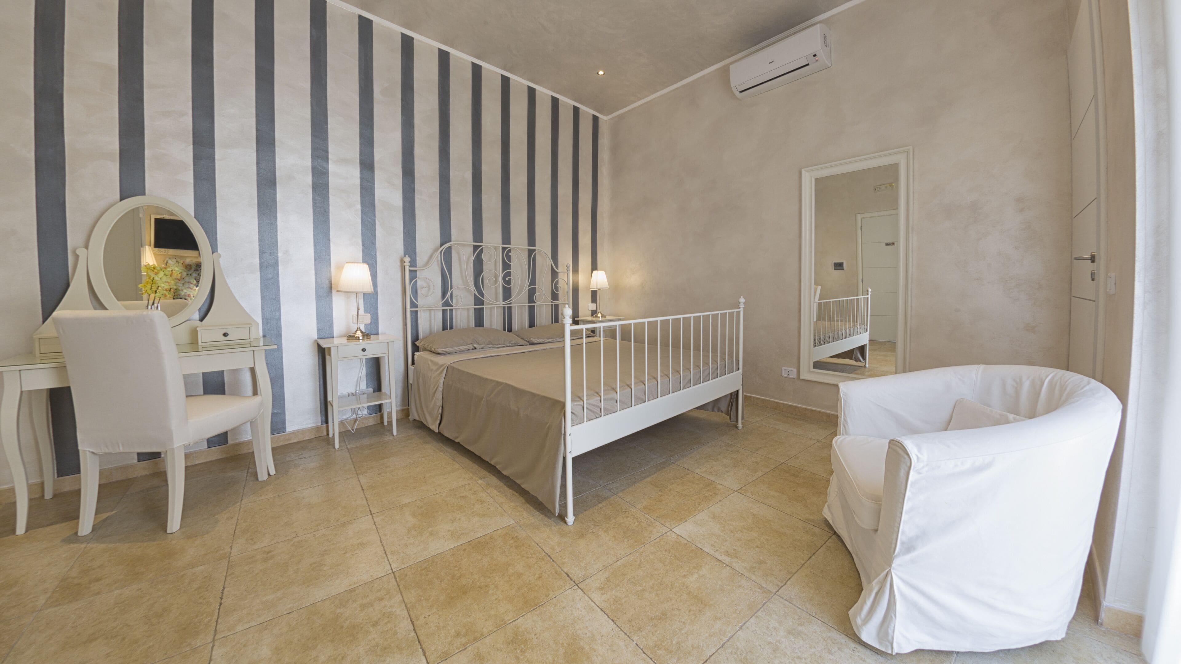 Un dormitorio con cama, escritorio, silla, espejo y mesita de noche.