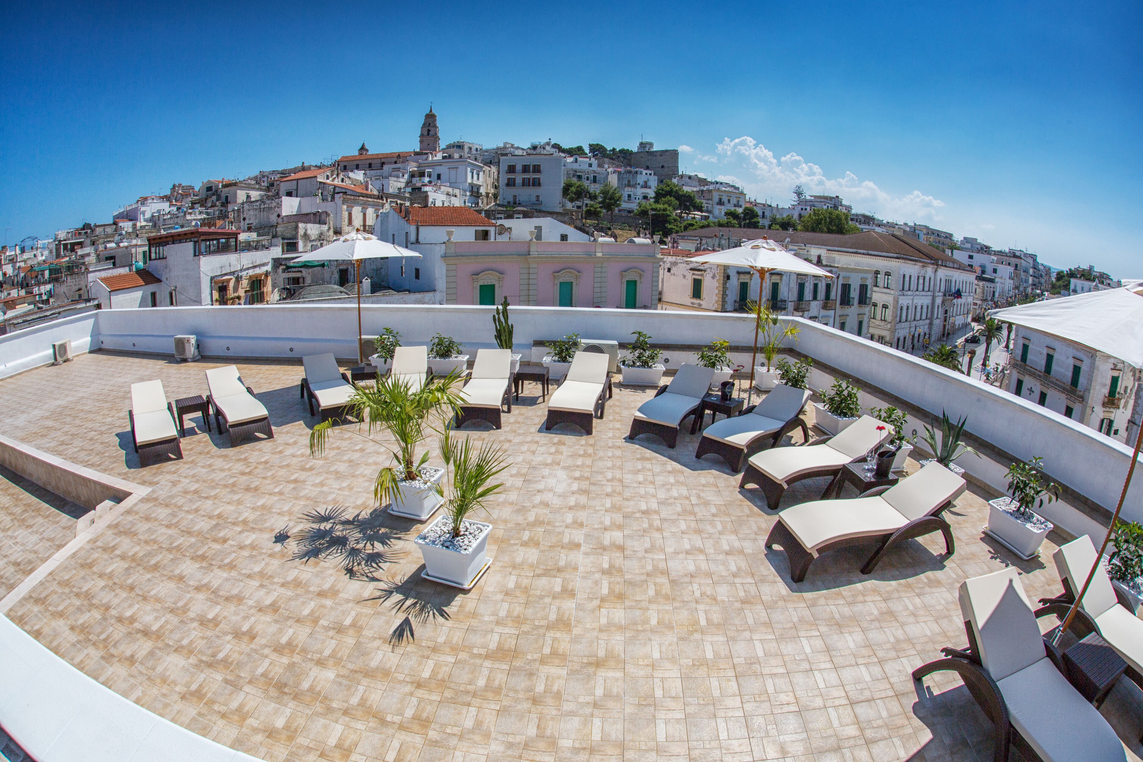 A rooftop terrace with sun loungers, potted plants, and a view of a historic town.