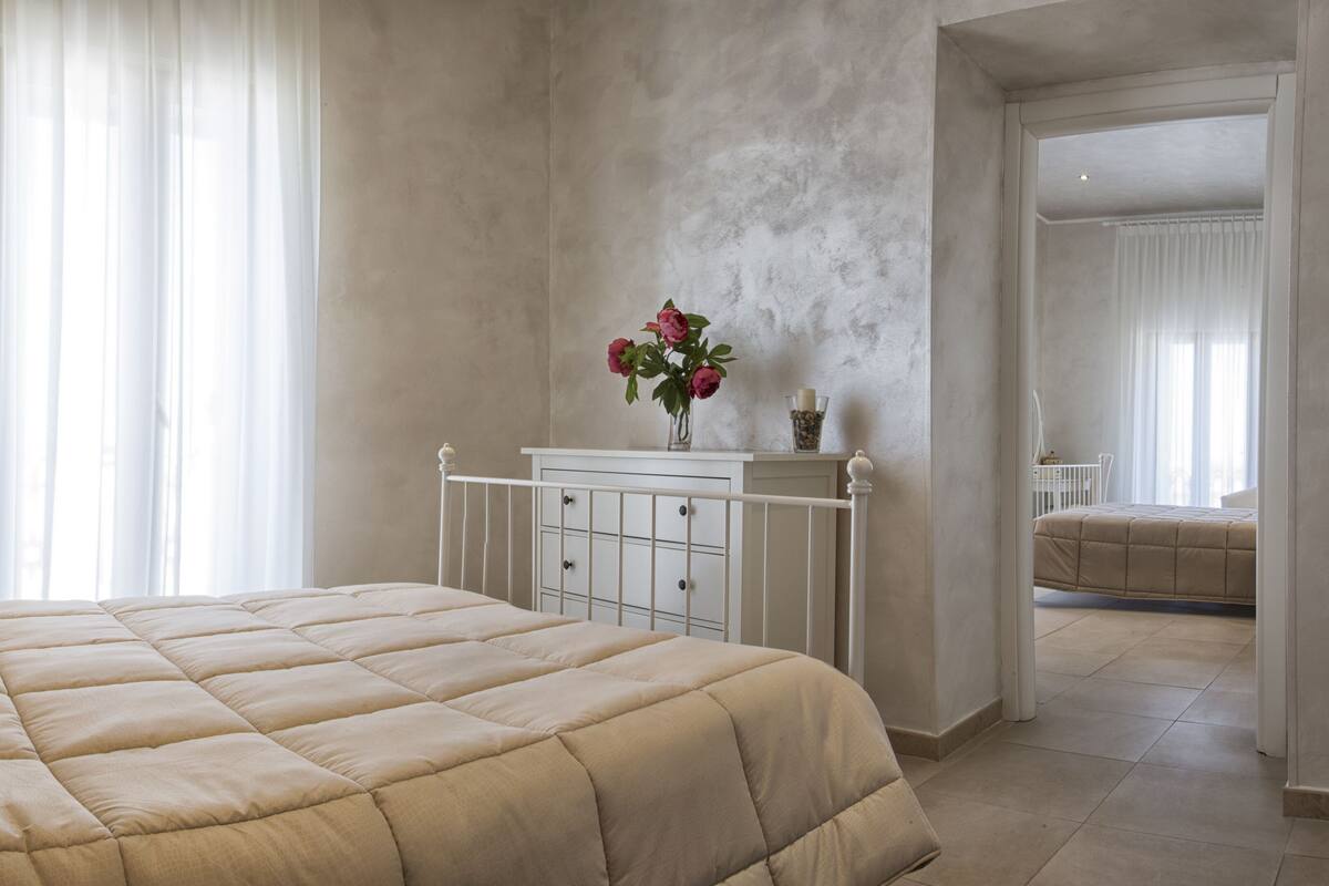 A bedroom with a large bed, a dresser, and a vase with flowers.