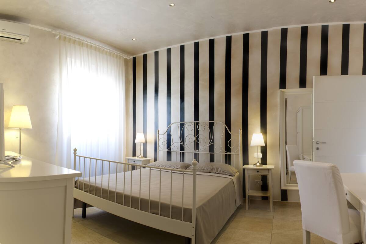 A bedroom with a curved ceiling, a bed with a metal frame, bedside tables with lamps, a desk, and a chair.
