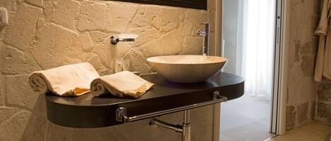Un baño con pared de piedra, un espejo grande, un lavamanos y un inodoro.
