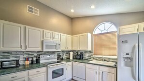 Una cocina con armarios blancos, microondas, estufa, horno y refrigerador.