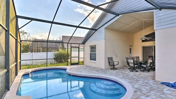 Una piscina con borde de azulejos y un patio con sillas y una mesa.
