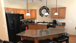A kitchen with wooden cabinets, a black refrigerator, a granite island with bar stools, and pendant lighting. - Convenient Park City Condo (Park City)