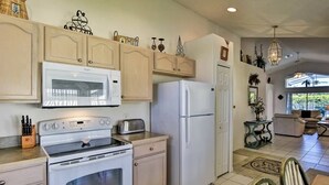 A kitchen with a microwave, stove, refrigerator, and a dining area with chairs and a table. - Achieve your Magical Vacation! 12 Mins to Disney! (Kissimmee)