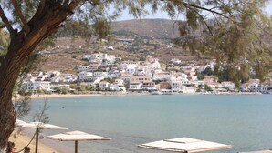 A coastal town with white buildings, a beach with umbrellas, and a clear view of the sea. - Bella Vista Design Studios (Andros)