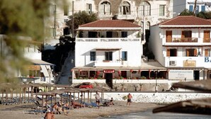 A beach with sun loungers and a building with a balcony. - Bella Vista Design Studios (Andros)