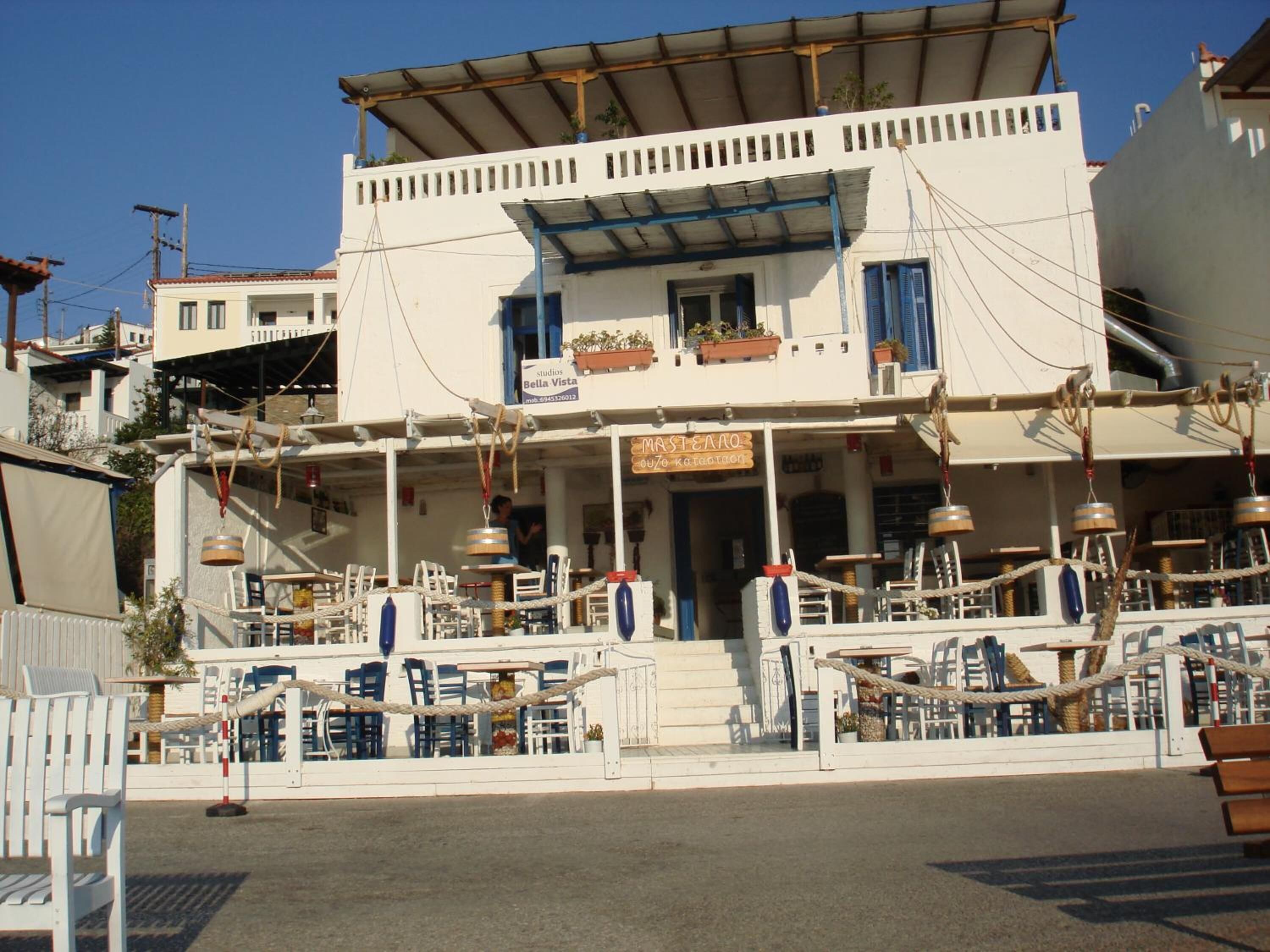 A two-story building with a balcony, outdoor seating area, and a sign for 'Bell Vista'.