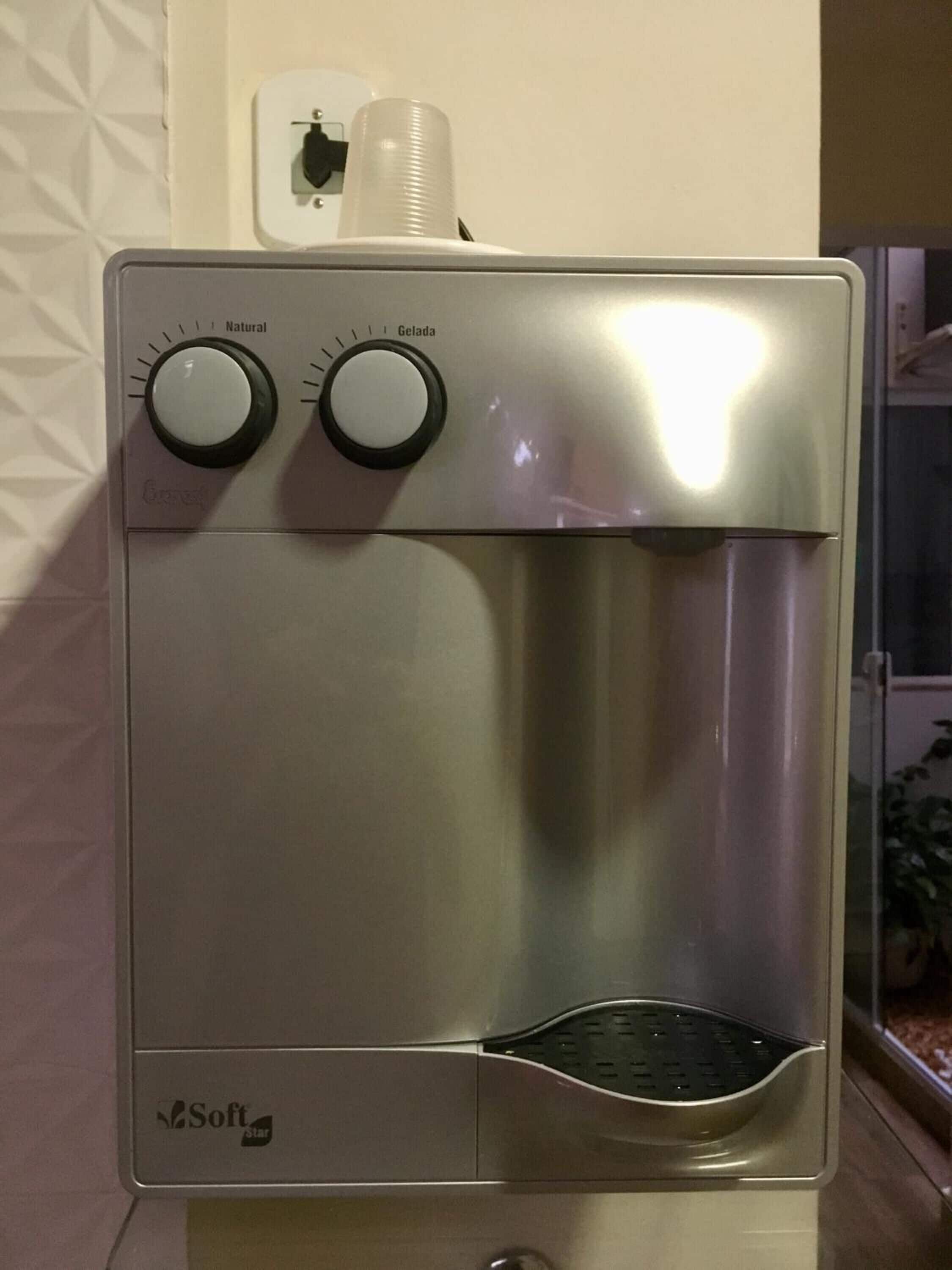 Un dispensador de agua con dos mandos etiquetados como 'Natural' y 'Gelada', y un portabotellas encima.