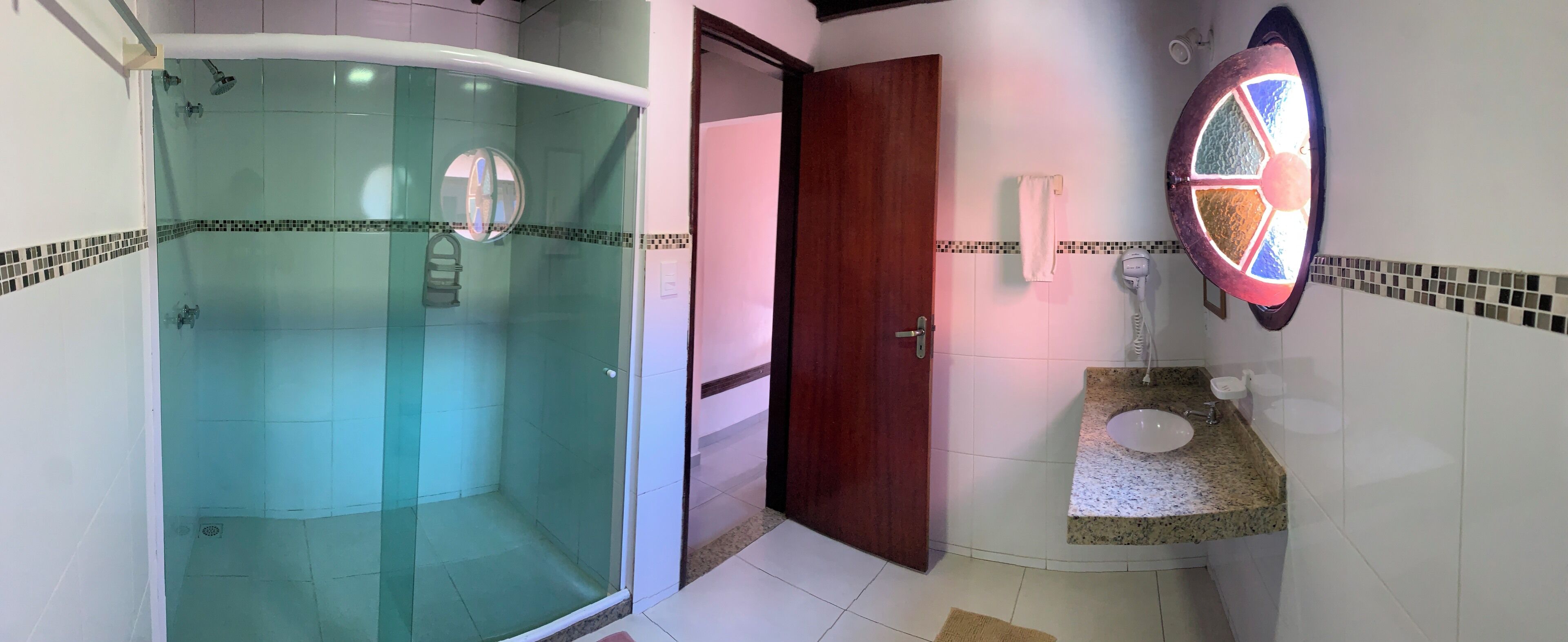 A bathroom with a glass-enclosed shower, a wooden door, a sink with a mirror, and tiled walls.