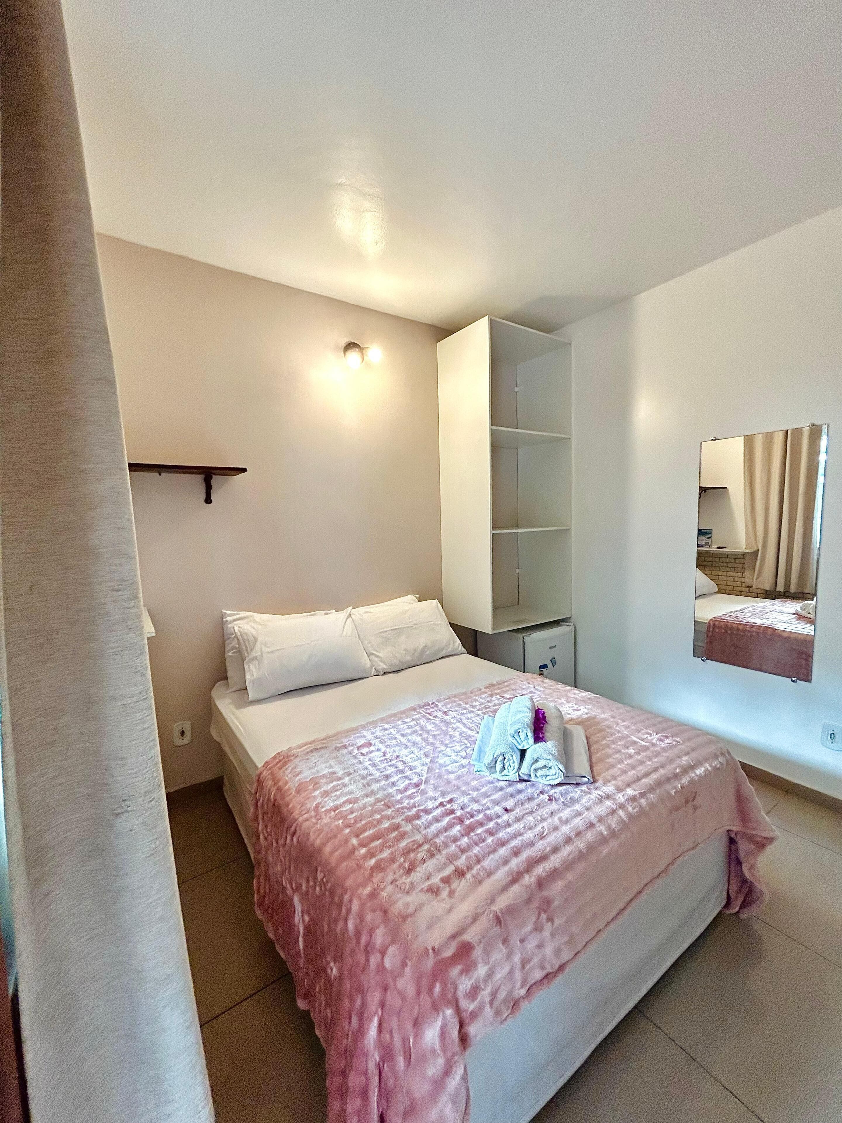 A bedroom with a bed, a bedside table, a mirror, and a wardrobe.