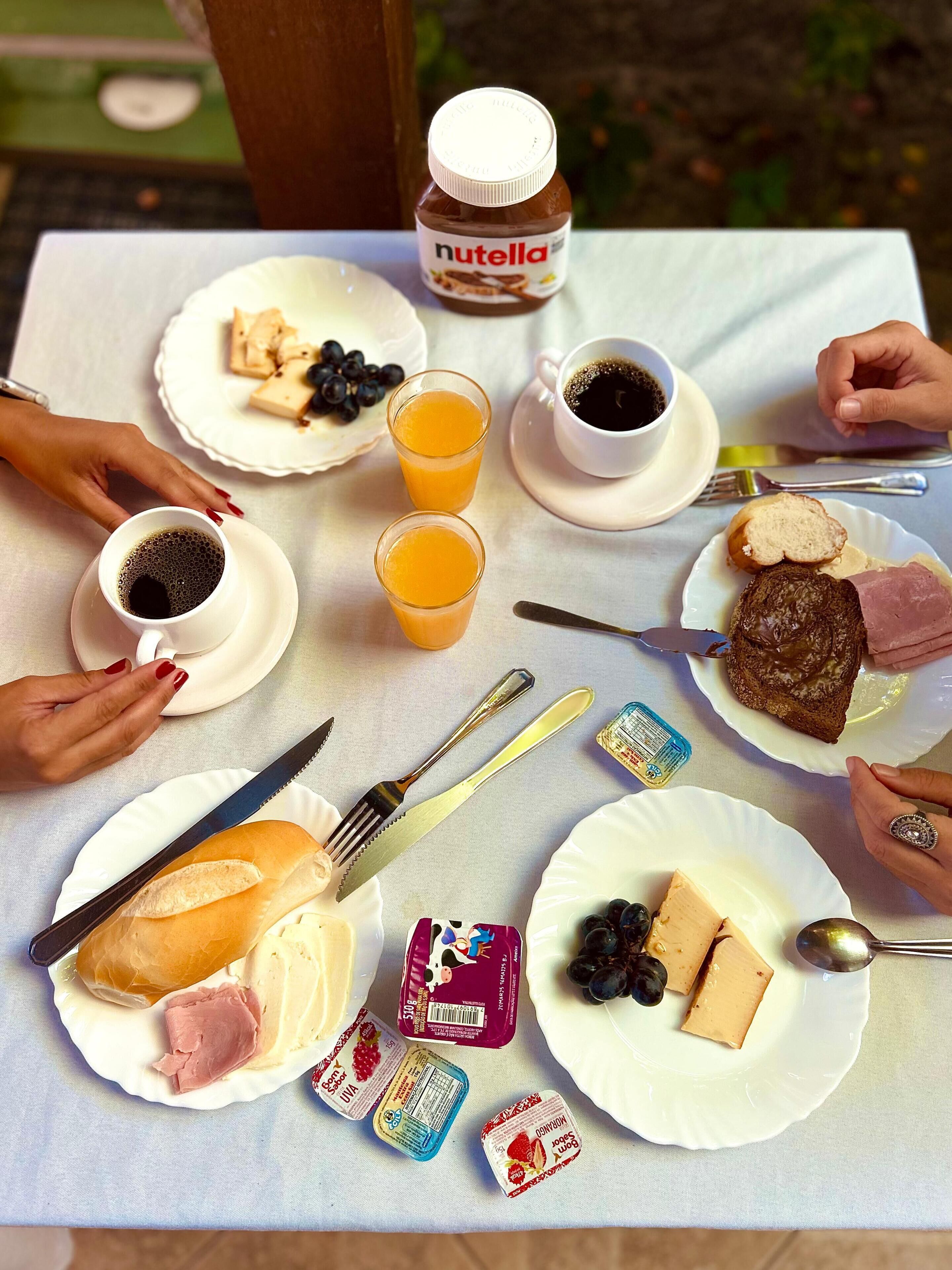 A table set with various breakfast items including bread, cheese, jam, and a Nutella jar.