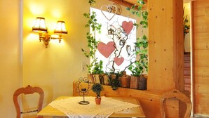 Una habitación acogedora con vigas de madera, una mesa con mantel de encaje, dos sillas con cojines rojos y luces fijadas a la pared.