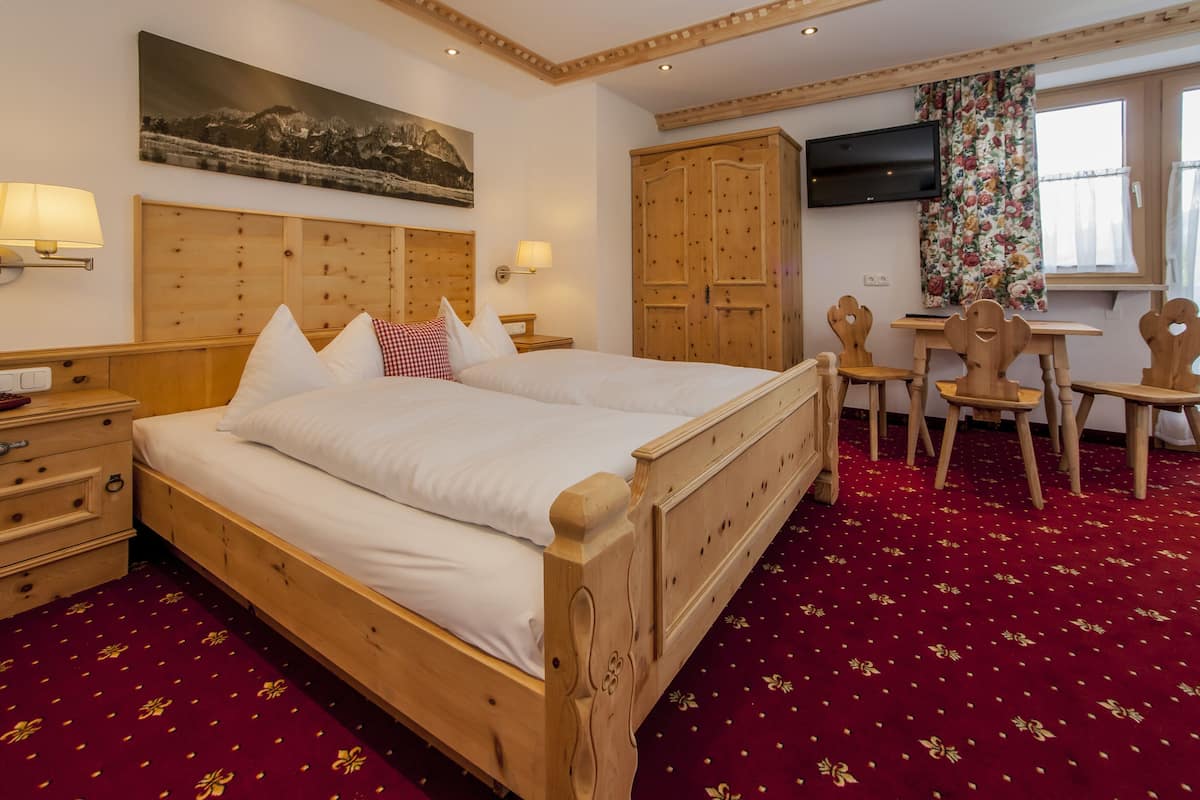 A hotel room with a wooden bed, a desk with chairs, a television, and a large window with curtains.