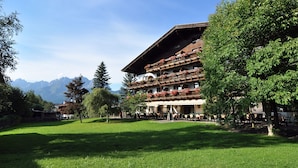 Un hotel de varios pisos con balcones, un patio con césped y montañas al fondo.